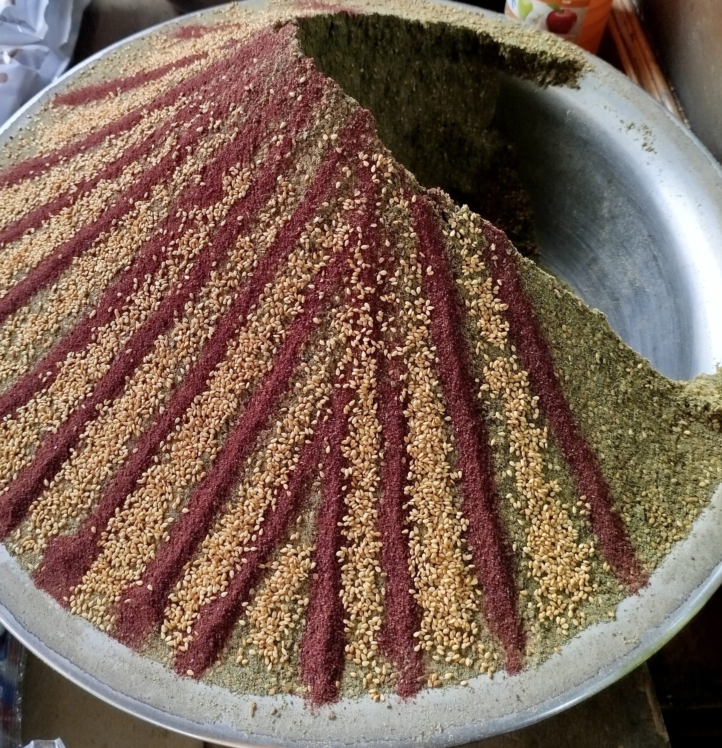 A mound of dried za'atar in a large metal tray, decorated with stripes of sumac and sesame, Palestine